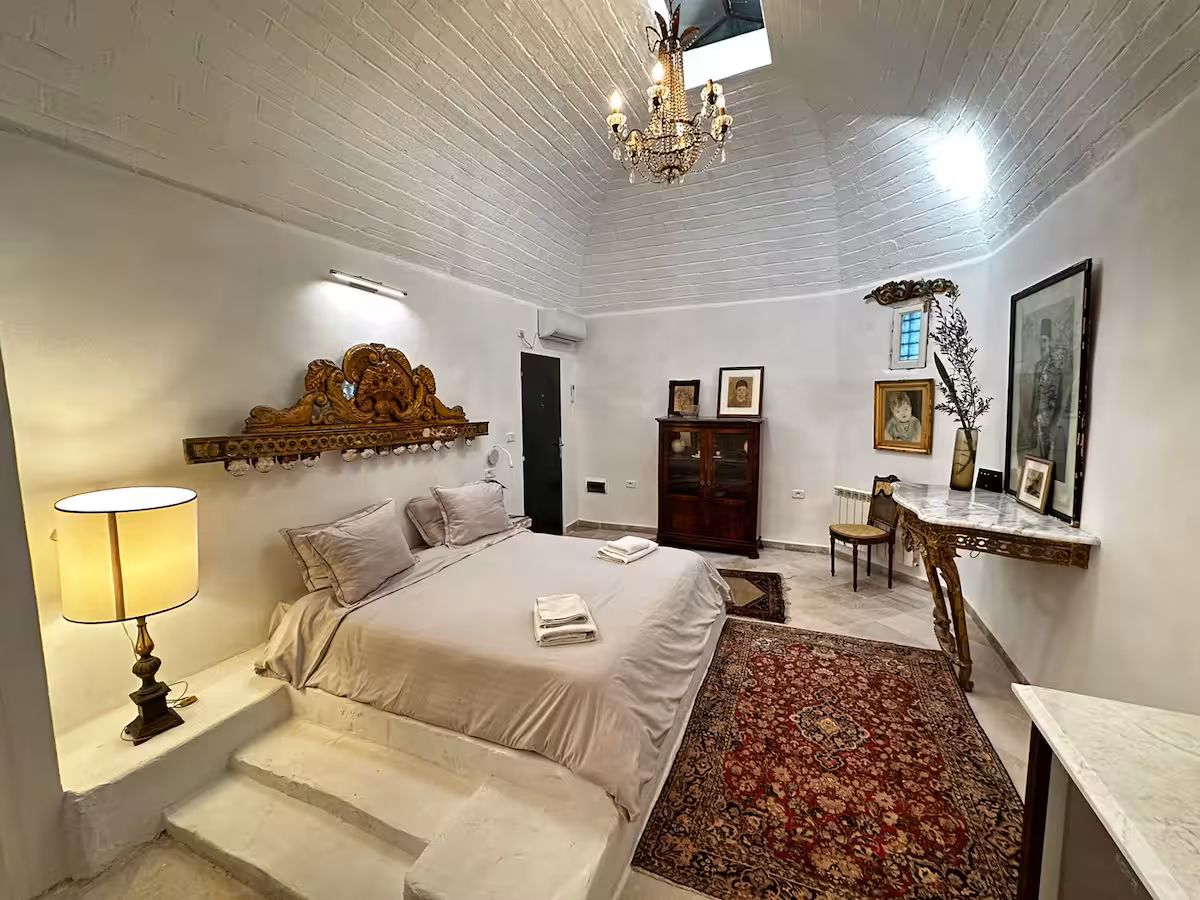 Chambre de la suite Si Ibrahim sous sa voûte de pierre, tête de lit sculptée dorée et tapis ancien